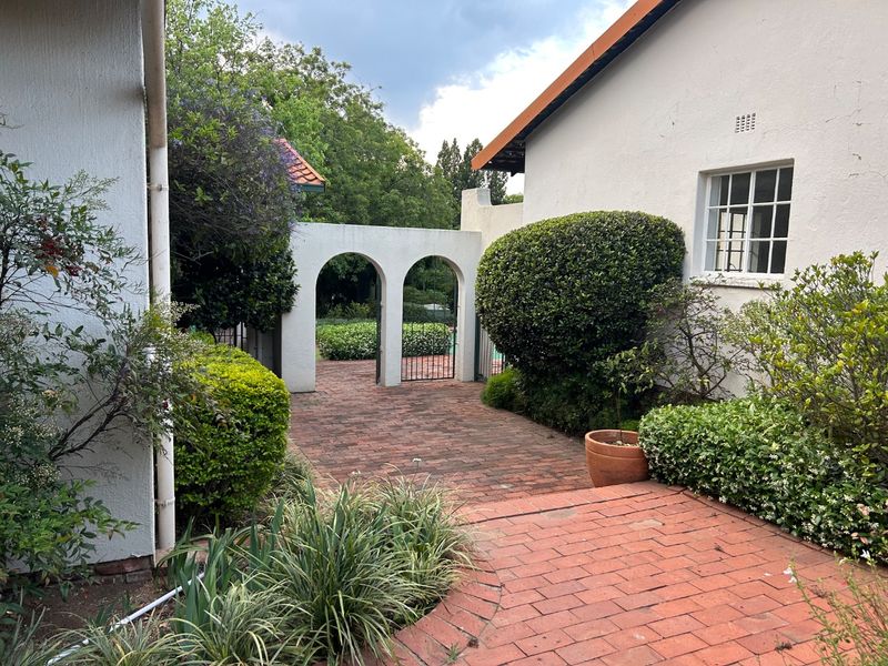 A charming rear courtyard featuring brick paving, a decorative arched gateway, and established garden landscaping between two building sections.