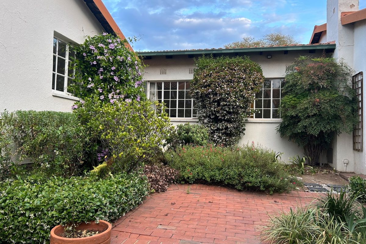 A private rear courtyard featuring a brick-paved patio area surrounded by established garden beds and mature shrubbery against the building facade.