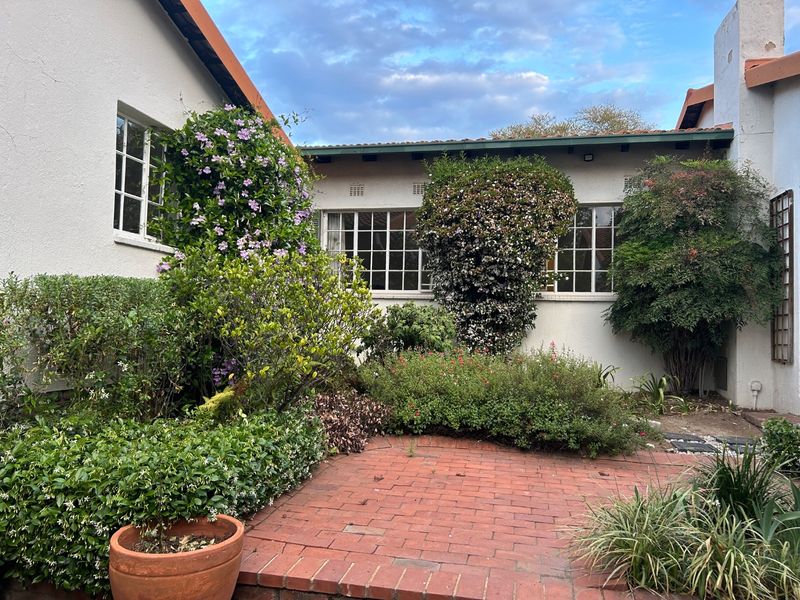 A private rear courtyard featuring a brick-paved patio area surrounded by established garden beds and mature shrubbery against the building facade.