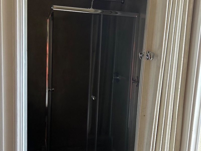 A compact bathroom featuring a modern glass shower enclosure and a folding door entrance.