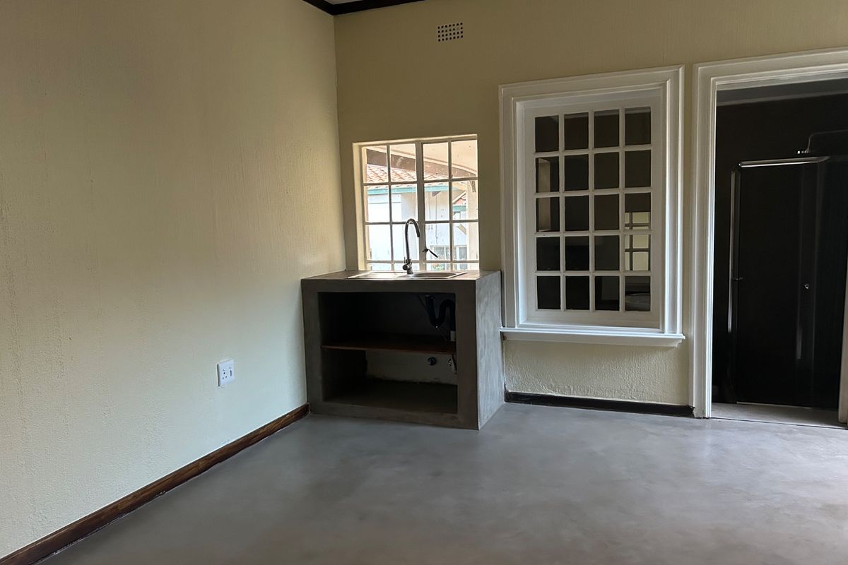 A minimalist kitchen area featuring a custom concrete sink unit, polished concrete flooring, and classic lattice windows.