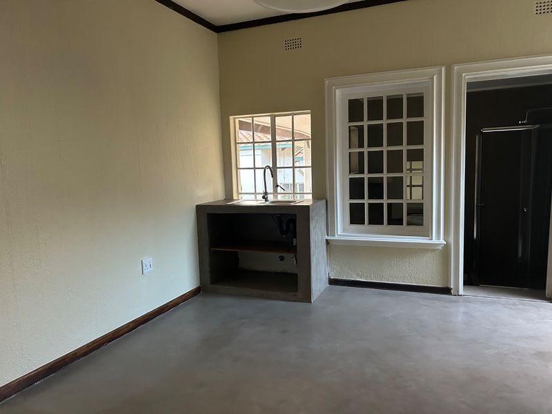 A minimalist kitchen area featuring a custom concrete sink unit, polished concrete flooring, and classic lattice windows.