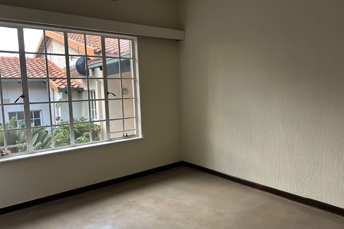 An empty bedroom featuring concrete flooring, steel-framed windows, and neutral walls, providing a blank canvas for interior design.