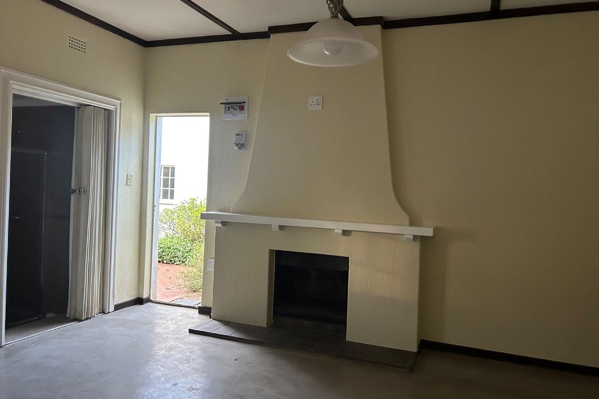 An empty living room featuring a built-in fireplace with a mantelpiece, exposed ceiling beams, and direct access to an outdoor area.