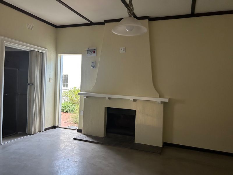 An empty living room featuring a built-in fireplace with a mantelpiece, exposed ceiling beams, and direct access to an outdoor area.