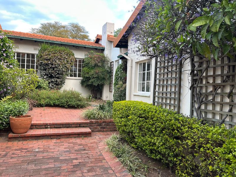 A charming rear courtyard featuring classic brick paving, tiered steps, and established garden landscaping with climbing plants against the building facade.