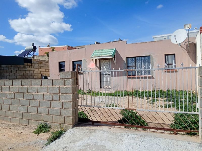 Front view of a single-story house featuring a metal security gate, concrete block boundary wall, and solar water heating system.