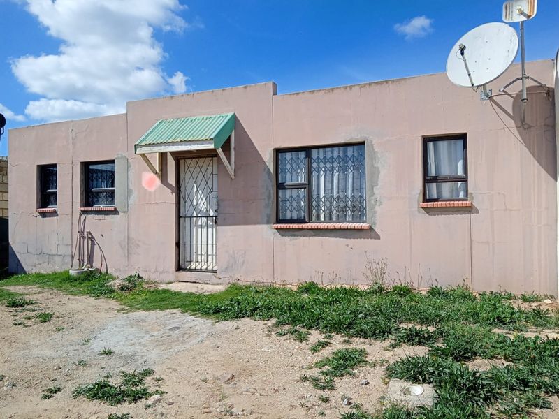 Front facade of a single-story house featuring security gates, burglar bars, and a satellite dish, with an unpaved front yard area.