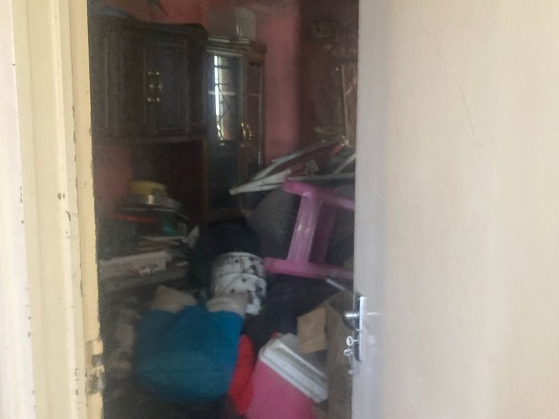 A cluttered utility or storage space featuring exposed ceiling rafters and worn wall finishes, requiring significant maintenance and clearing.