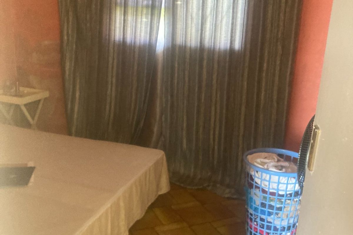 A bedroom featuring tiled flooring and a window with curtains, requiring cosmetic updates to the wall finishes.