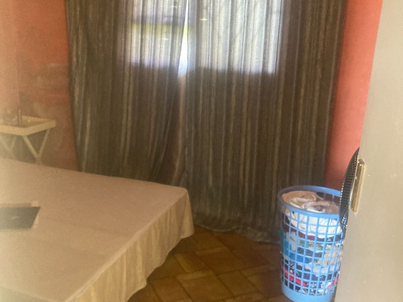 A bedroom featuring tiled flooring and a window with curtains, requiring cosmetic updates to the wall finishes.