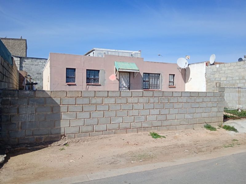 Front view of a single-story house featuring a concrete block boundary wall, security bars on windows, and a small entrance awning.