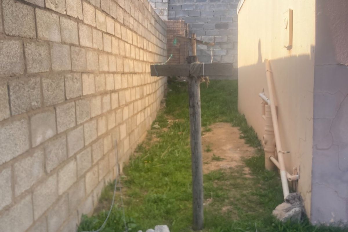 A narrow side or rear exterior passage featuring a concrete block boundary wall and plastered building exterior with visible surface cracks.