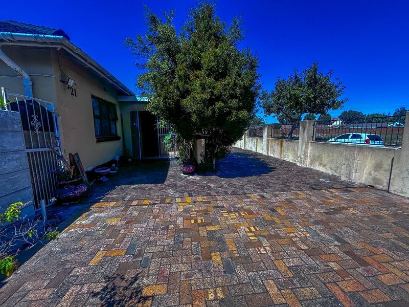 Front exterior view featuring a paved driveway, boundary wall, and security gate access to the property entrance.