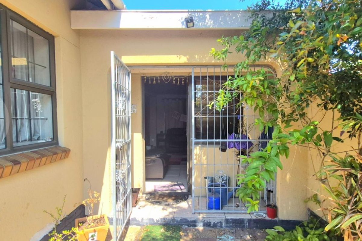 Rear exterior view of the property featuring a paved patio area, security gate, and access to the interior living space.