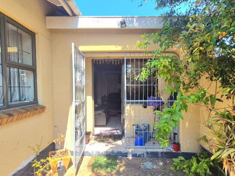Rear exterior view of the property featuring a paved patio area, security gate, and access to the interior living space.