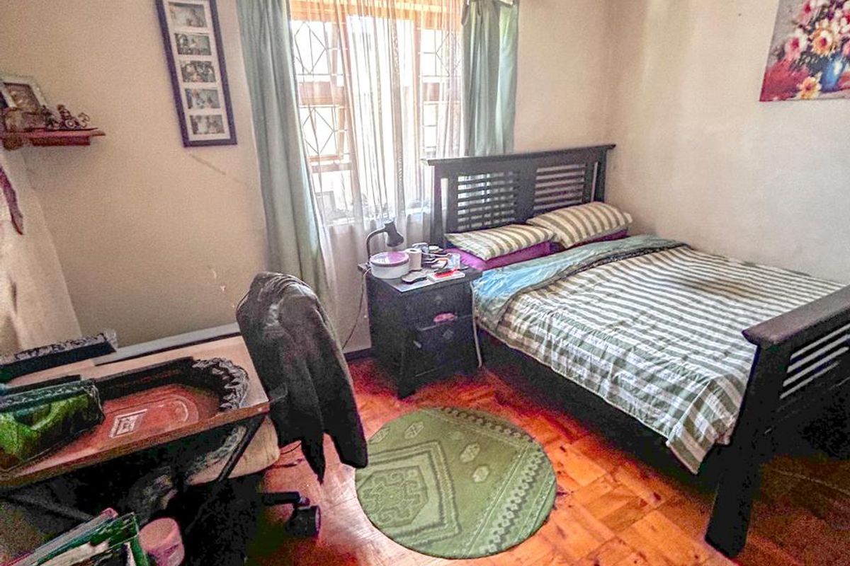 A bedroom featuring parquet flooring, a ceiling fan, and security bars on the window. The ceiling shows signs of staining.