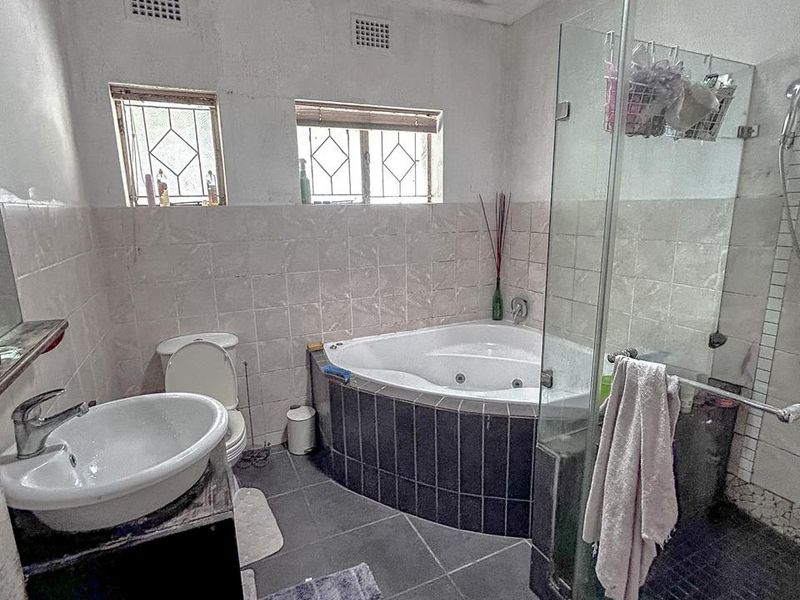 A dated bathroom featuring a corner spa bath, glass shower enclosure, vanity basin, and toilet, requiring cosmetic updates to the ceiling and finishes.