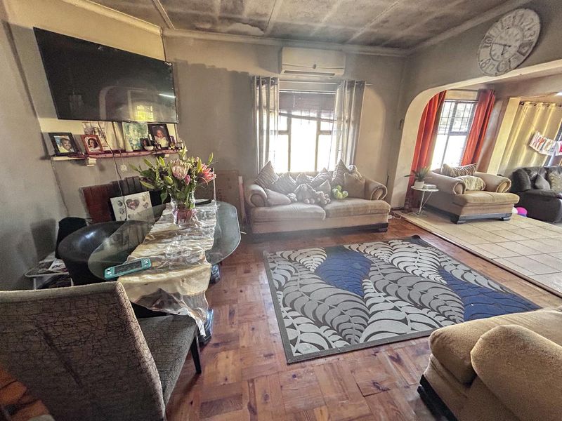 Open-plan living area featuring parquet flooring, an archway transition to an adjacent space, and a wall-mounted air conditioning unit.