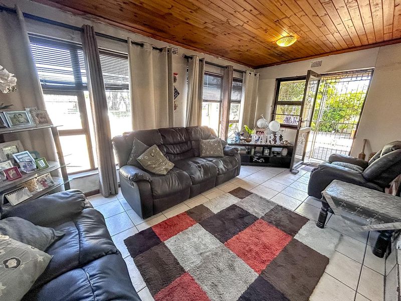 A living room featuring a warm timber tongue and groove ceiling, ceramic tiled flooring, and large windows providing natural light with direct access to the exterior.