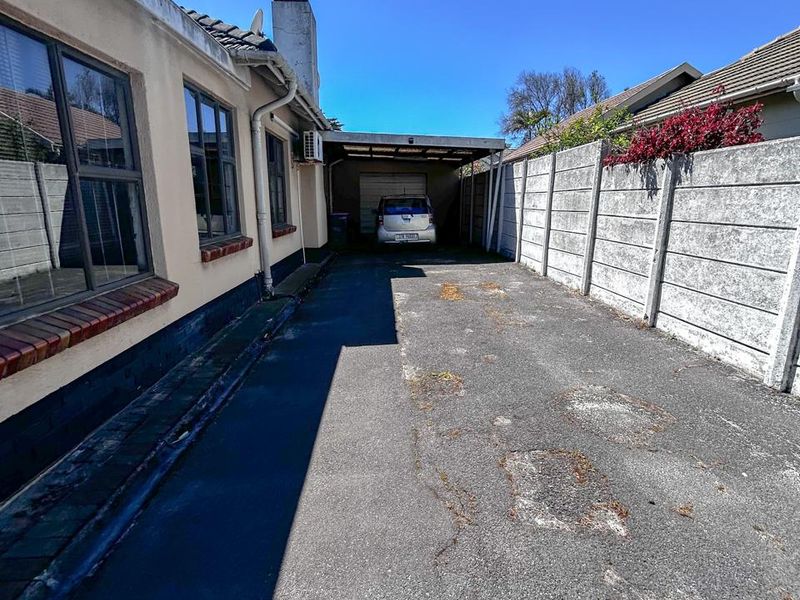 Rear exterior view showing a paved driveway, carport, and precast concrete boundary wall along the side of the house.