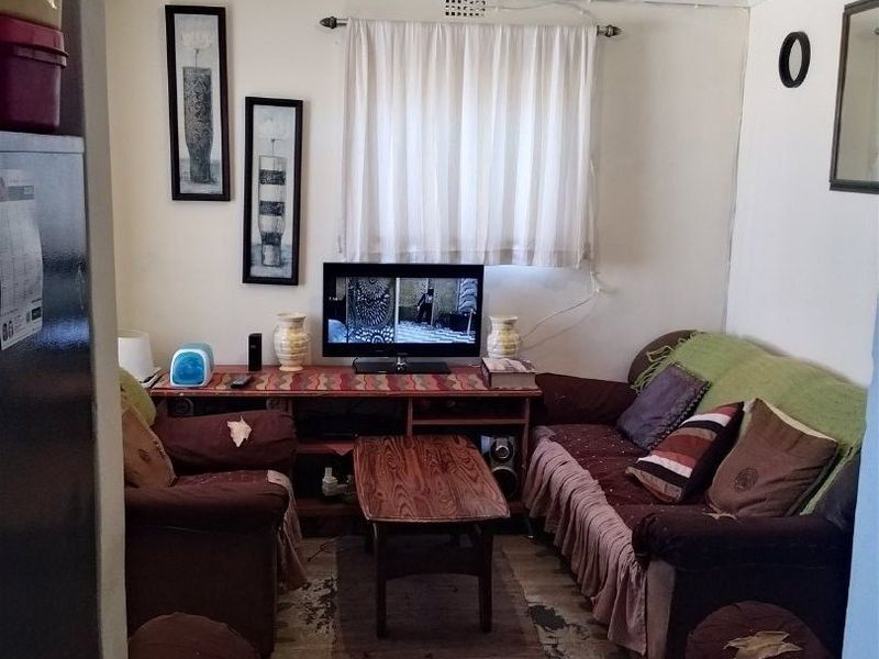 A compact living room area featuring basic finishes, requiring cosmetic updates to improve the overall condition and appeal of the space.