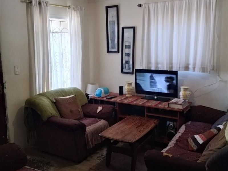 A compact living room featuring tiled flooring and ceiling panels, offering a functional space that could benefit from cosmetic updates and improved lighting.