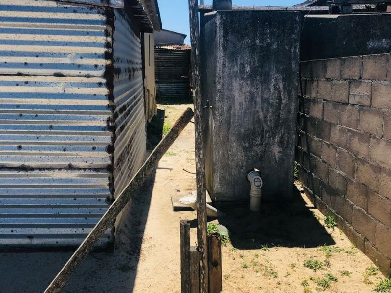 Rear exterior area featuring corrugated iron structures, a concrete water tank, and boundary walling with weathered finishes and exposed sandy ground.