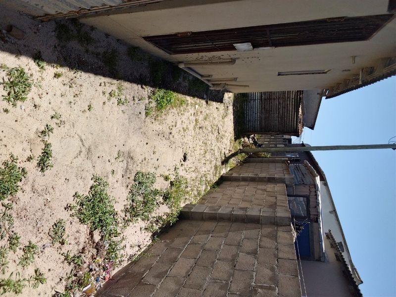 A narrow side or rear yard area featuring a concrete block boundary wall and unpaved ground requiring landscaping and maintenance.