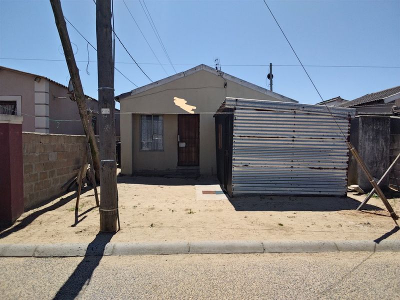 Front view of a single-story house featuring a corrugated iron structure in the yard and a security gate entrance.