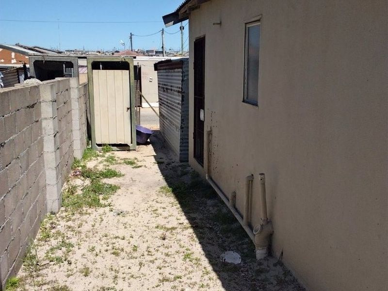 A narrow rear exterior area featuring a concrete block boundary wall, exposed external plumbing, and a small corrugated metal structure.