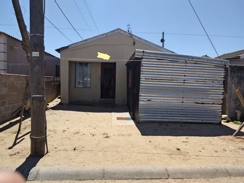 Front view of a residential property featuring a main dwelling with security bars and an adjacent corrugated iron structure on an unpaved lot.
