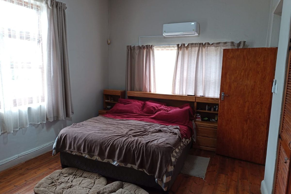 A bedroom featuring hardwood flooring, a built-in headboard with integrated bedside tables, and a wall-mounted split-system air conditioner.