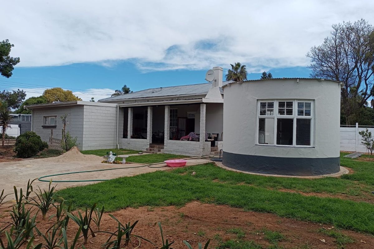 Rear view of a house featuring a covered patio, a distinctive circular room extension, and a concrete driveway leading to the garden area.