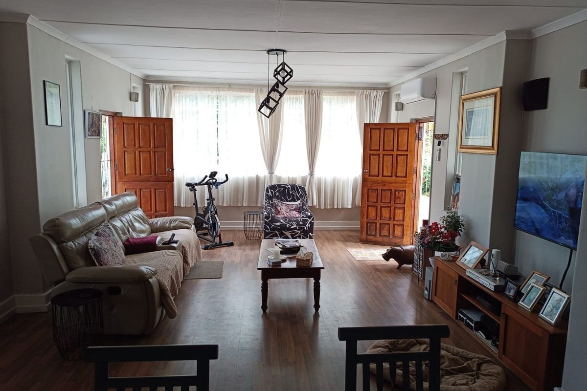 Spacious living room featuring laminate flooring, air conditioning, and dual timber panel doors leading to the exterior.