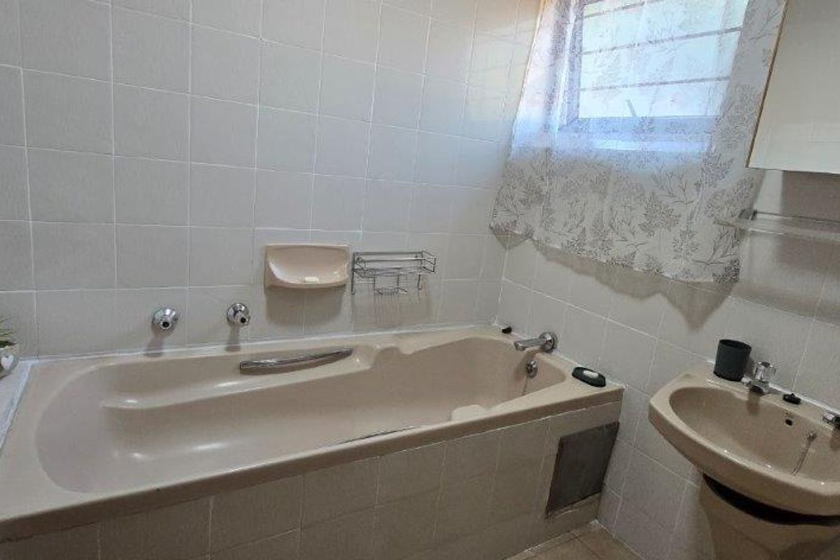 A functional bathroom featuring a built-in bathtub, pedestal washbasin, and tiled walls, offering a dated aesthetic ready for modernization.