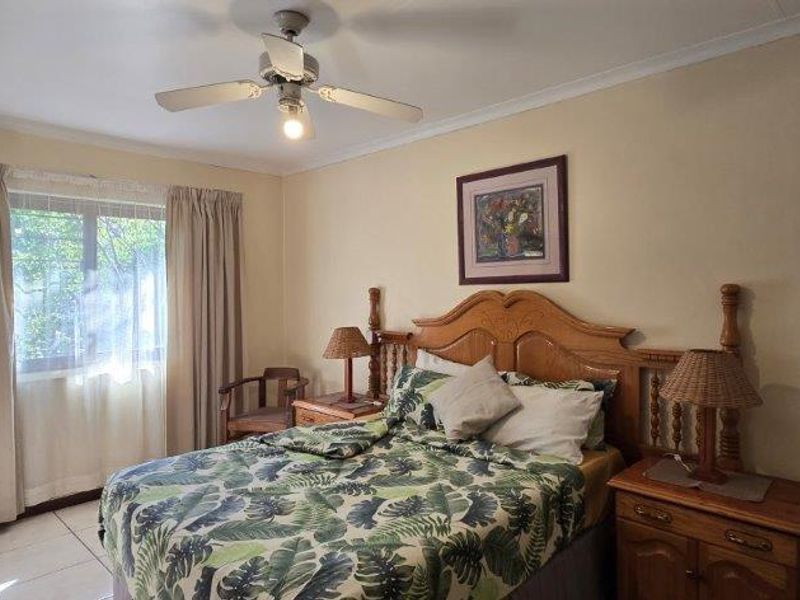 A bedroom featuring tiled flooring, a ceiling fan, and a window with curtains.