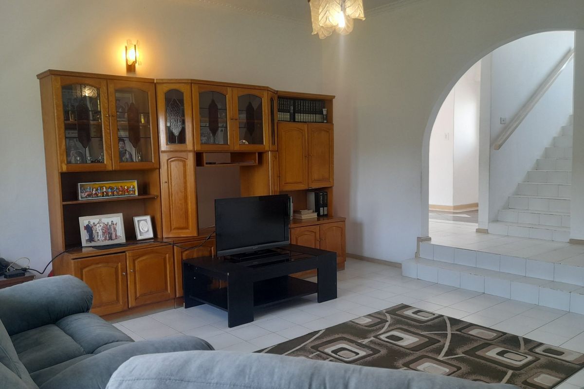 Spacious living area featuring tiled flooring, an elegant arched doorway leading to a staircase, and integrated wall lighting.