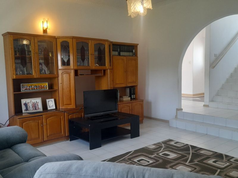 Spacious living area featuring tiled flooring, an elegant arched doorway leading to a staircase, and integrated wall lighting.