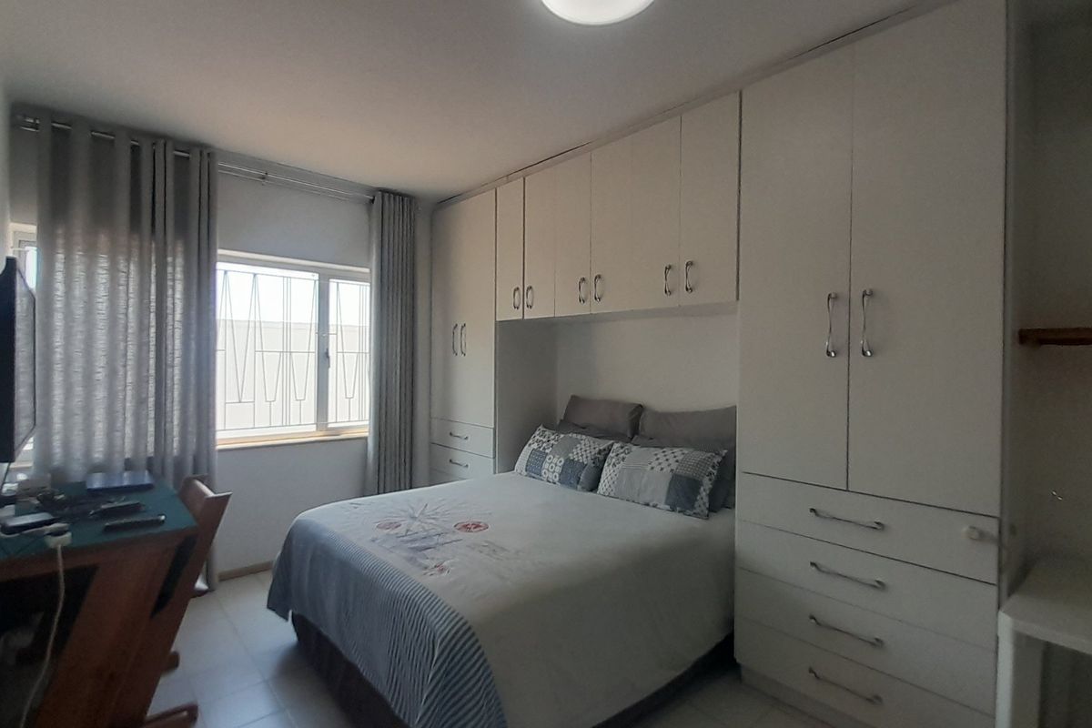A functional bedroom featuring extensive built-in cabinetry, an integrated air conditioning unit, and security bars on the window.