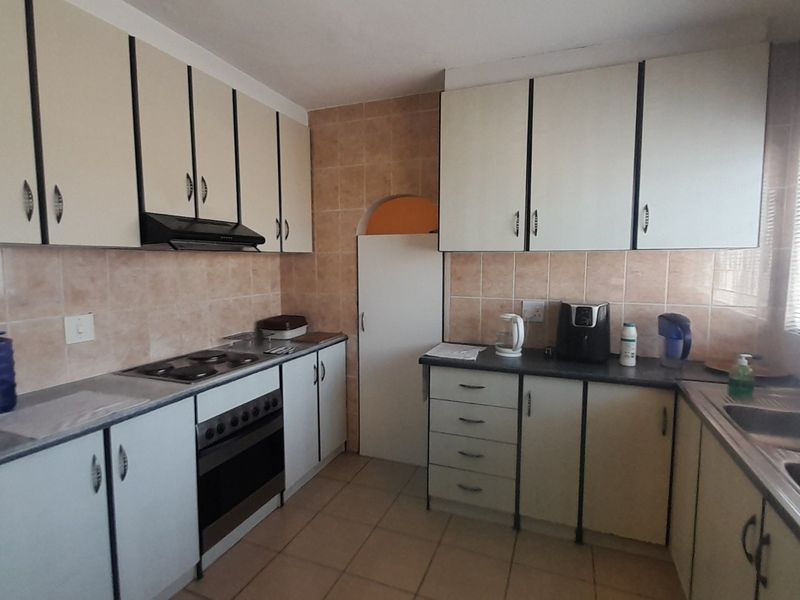 A functional kitchen featuring built-in cabinetry, an electric hob with extractor fan, tiled splashbacks, and a double sink with tiled flooring.