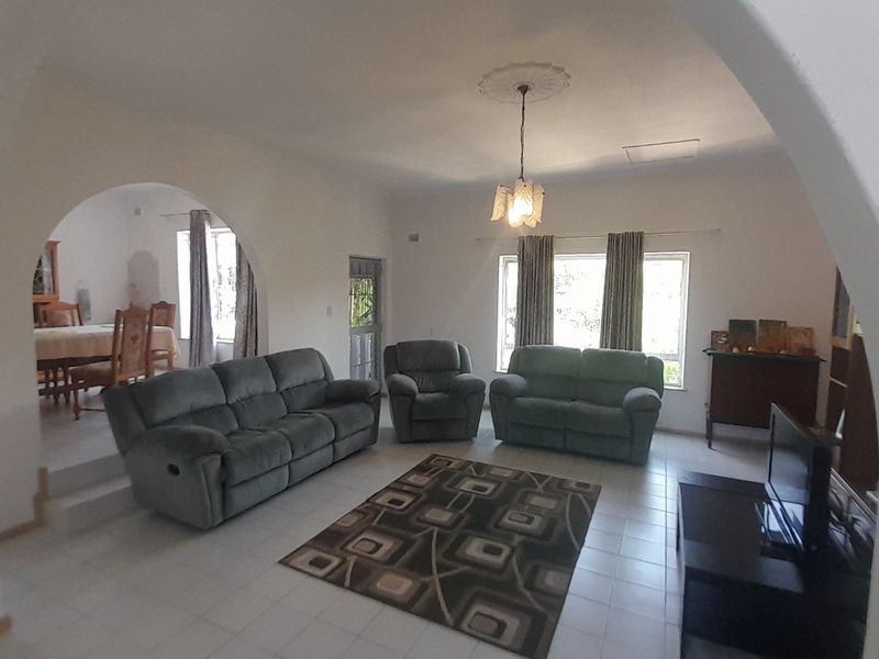 Spacious open-plan living and dining area featuring arched architectural details, tiled flooring, and a central ceiling rose with pendant lighting.