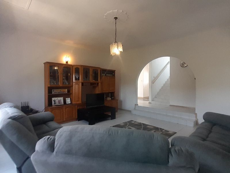 A spacious living room featuring a decorative ceiling rose, tiled flooring, and a distinctive arched entryway leading to a staircase.