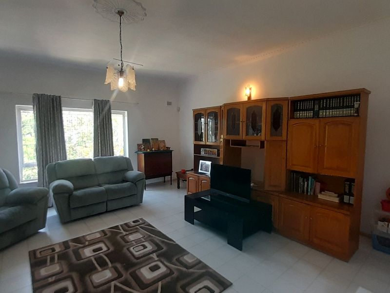 A spacious living room featuring tiled flooring, a decorative ceiling rose, and a large built-in wooden wall unit for storage.