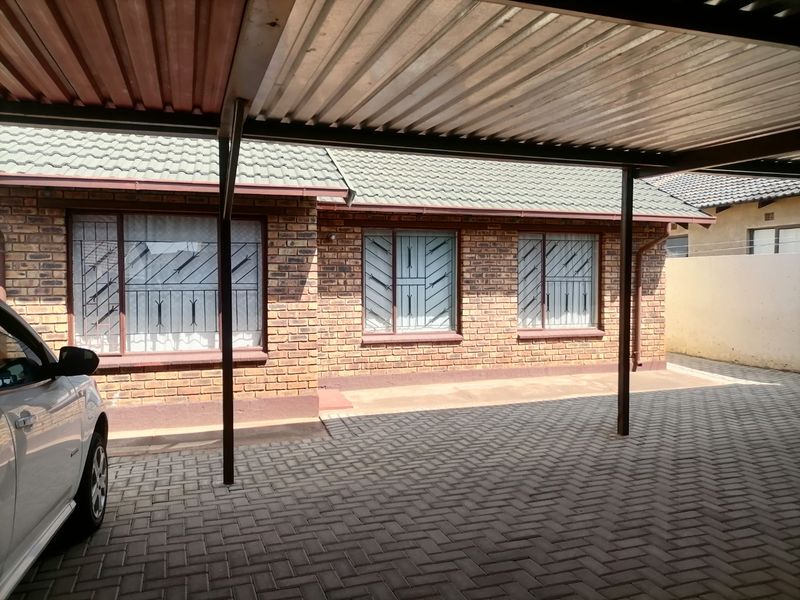 Front exterior view of a brick house featuring a covered carport, paved driveway, and security bars on the windows.