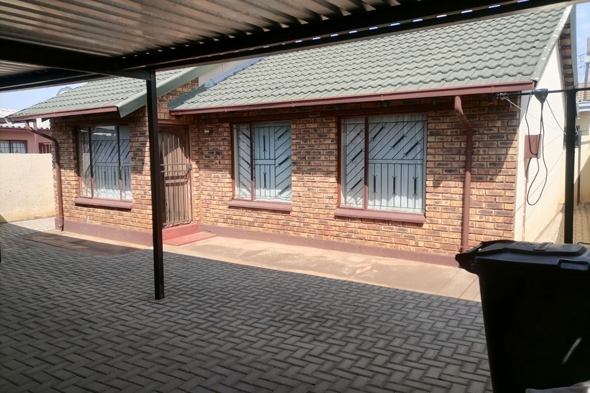 Rear exterior view of a face brick house featuring a covered patio area, paved flooring, and secure window bars.