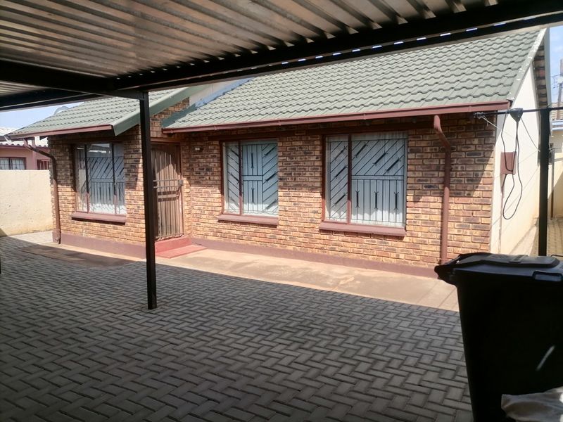 Rear exterior view of a face brick house featuring a covered patio area, paved flooring, and secure window bars.