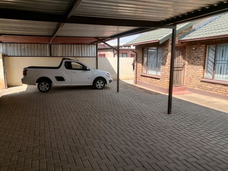 A covered carport area with paved flooring adjacent to a brick-faced residential building.