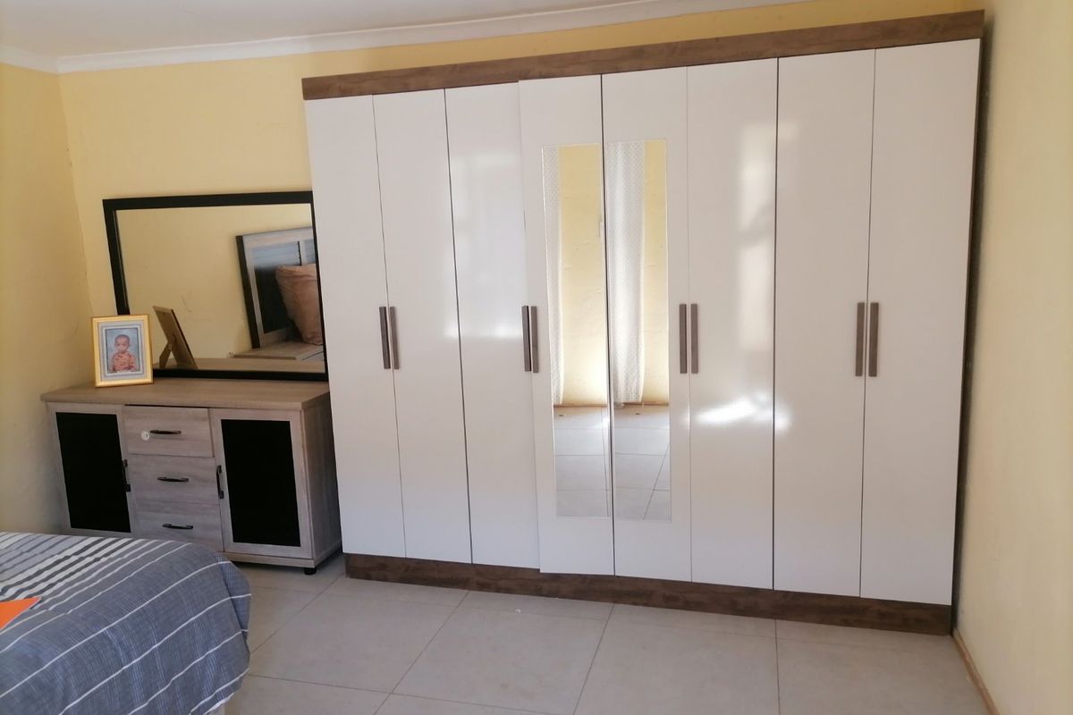A bedroom featuring a large, modern white built-in wardrobe with mirrored panels and neutral tiled flooring.