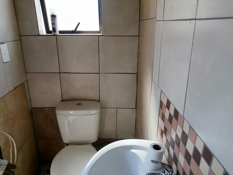 A compact bathroom featuring a standard toilet, washbasin, and tiled wall finishes with a small top-hung window for ventilation.